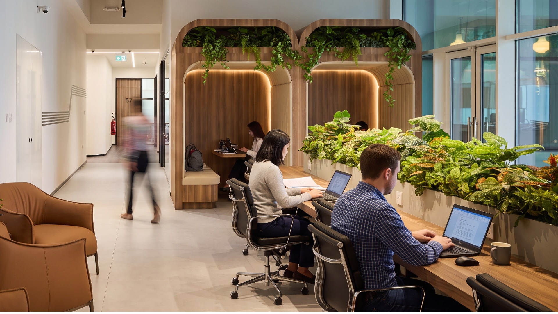 The coworking floor at flowork Business Bay, people working at desks along a planted window bench with wooden booths beyond